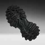 A single black rugged outsole or shoe tread shown floating against a smooth gray gradient background.
