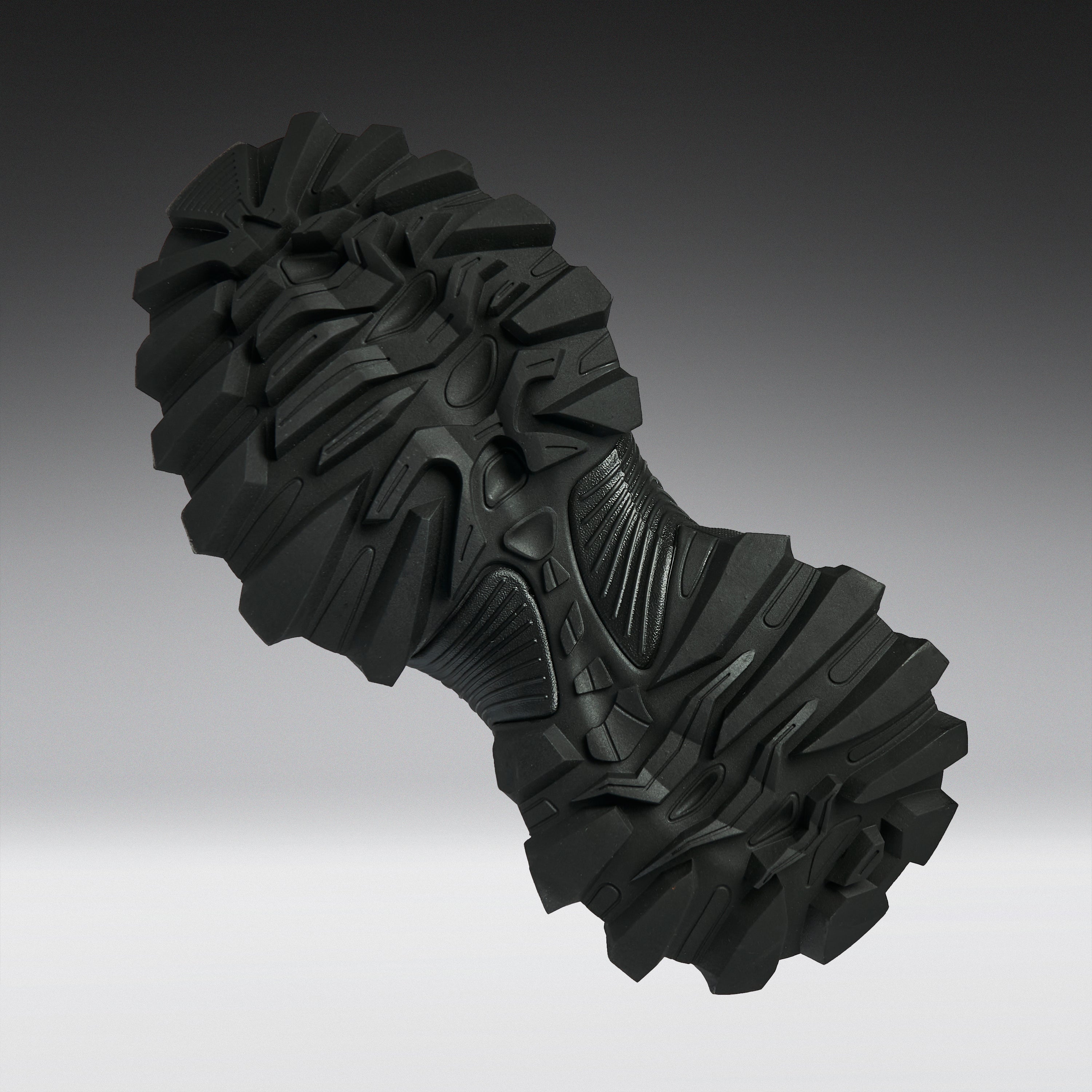 A single black rugged outsole or shoe tread shown floating against a smooth gray gradient background.