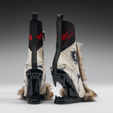 A pair of high-heeled boots shown from the back, featuring glossy black wedge heels with sharp teeth-like details, cream-colored panels with black graphic print, red paint splatter accents, and brown fur trim, photographed on a gray gradient studio background.