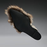 A black slip-on shoe with a brown and beige faux-fur trim, shown from a side profile against a dark gray gradient background.