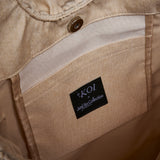 Close-up of the interior lining of a beige denim garment, showing a black brand label that reads 'KOI x Junji Collection' sewn onto a tan fabric pocket.