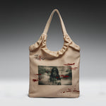 A beige canvas tote bag with a gathered top, featuring a graphic print of a dark-haired woman on the front, red splatter details, and Japanese text.