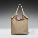 A beige canvas tote bag with gathered fabric trim along the top and dual shoulder straps, photographed against a dark-to-light gray gradient studio background.