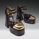 A pair of black platform high heels with gold metallic toe caps, red rhinestone studs, and double ankle straps. The insole of the front shoe features a printed illustration of an anime character.