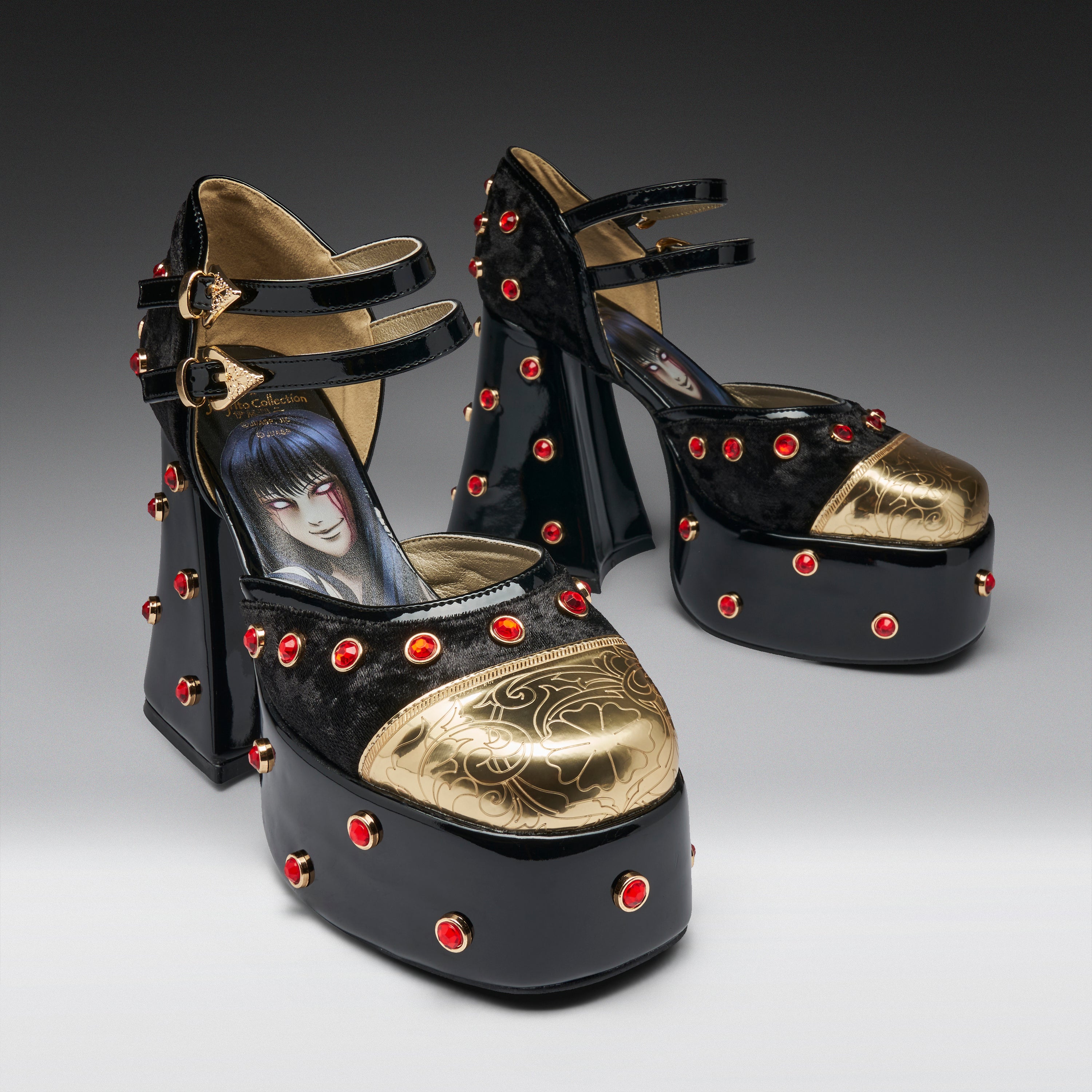 A pair of black platform high heels with gold metallic toe caps, red rhinestone studs, and double ankle straps. The insole of the front shoe features a printed illustration of an anime character.