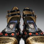 A pair of black and gold high-heeled platform shoes with red gem accents and an illustrated anime-style character printed on the insole, photographed against a dark gray gradient background.