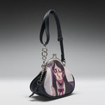 A black faux-leather coin purse featuring a printed anime illustration of a character with long dark hair and a red bow tie on the front flap. The purse has a silver-tone metal clasp, a black shoulder strap, and a hanging silver chain with a black tassel, photographed against a dark-to-light gray gradient studio background.