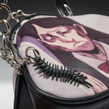 Close-up of a black handbag with a printed anime-style character design on the flap and a black centipede-shaped keychain attached to silver chain hardware.