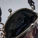 Close-up of the interior of a handbag showing a black fabric lining with a visible brand patch that reads 'Koi x Junji Ito Collection'. The bag has a silver-tone metal frame and chain details, with a dark patterned exterior partially visible at the bottom right.