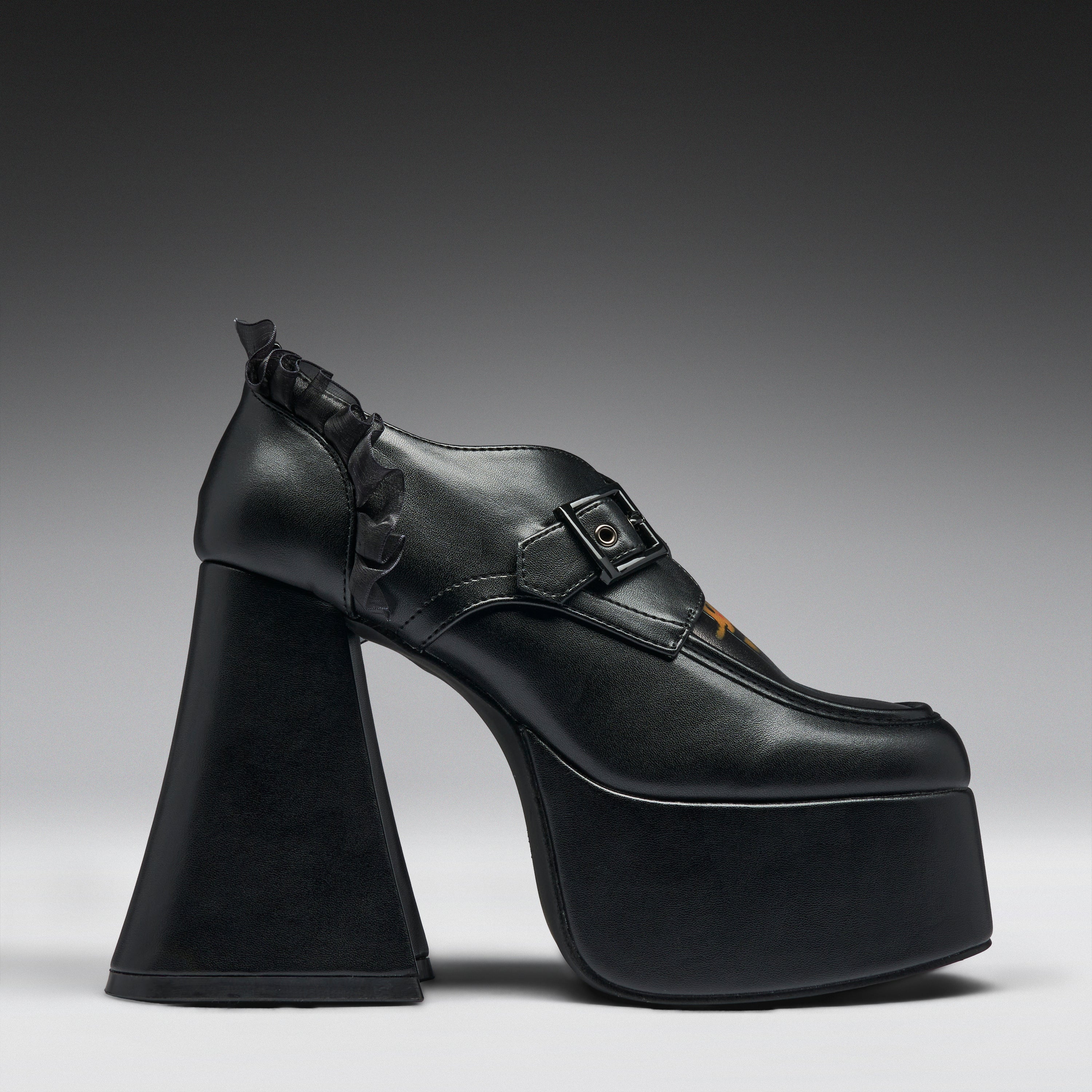 A single black platform high-heel shoe with a chunky sculptural block heel, a buckle strap across the instep, and a small orange accent near the toe, photographed against a dark-to-light gray gradient studio background.