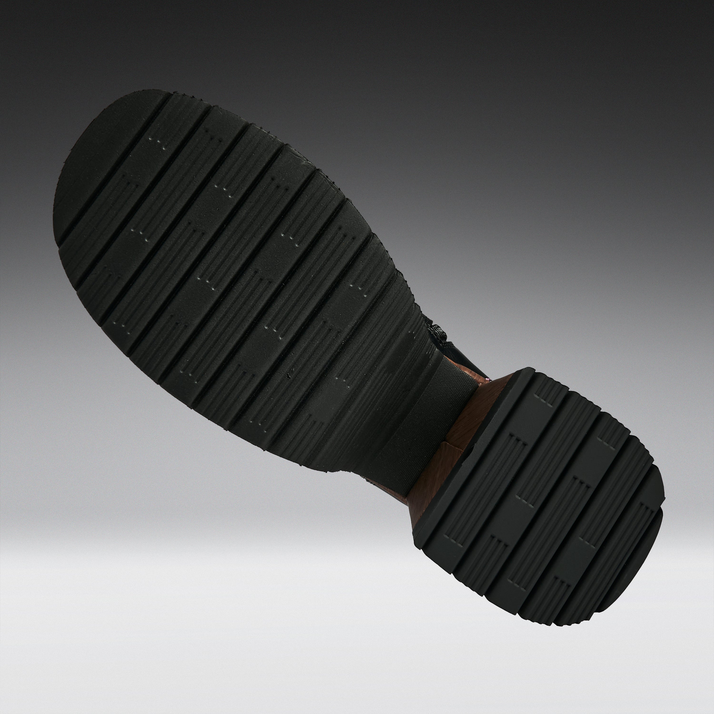 A close-up of a black rubber shoe sole with deep grooves, shown against a gradient gray background.