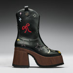 A black leather cowboy boot with a chunky brown wooden block heel and platform sole, decorated with embroidered stars, bows, and lightning bolts in red, yellow, and white.