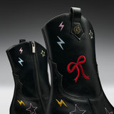 Black leather boots with embroidered lightning bolts and stars in multiple colors, featuring a red bow embroidery on the front boot.