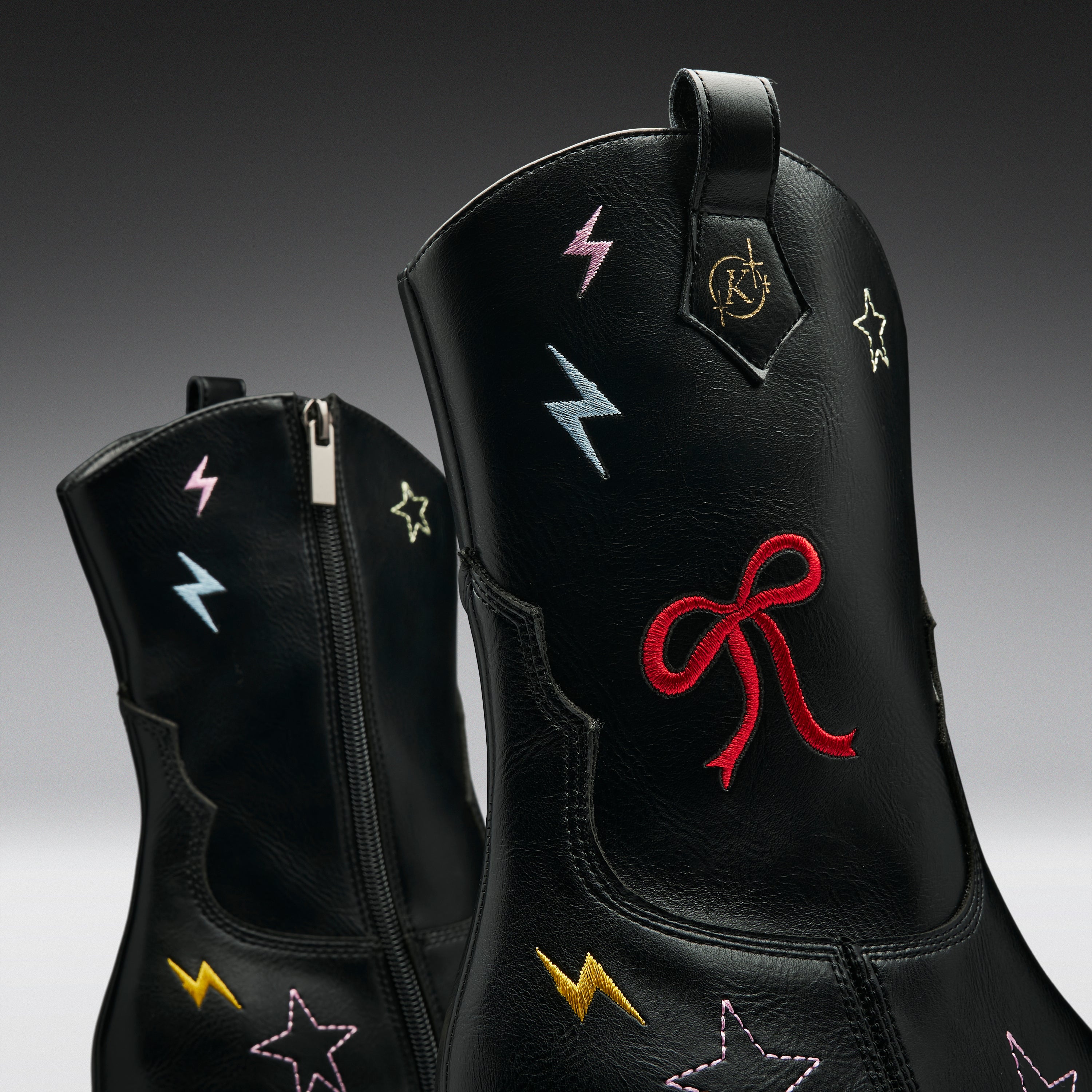 Black leather boots with embroidered lightning bolts and stars in multiple colors, featuring a red bow embroidery on the front boot.