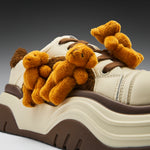 White sneaker with brown accents featuring small teddy bears and a bow on a gradient background