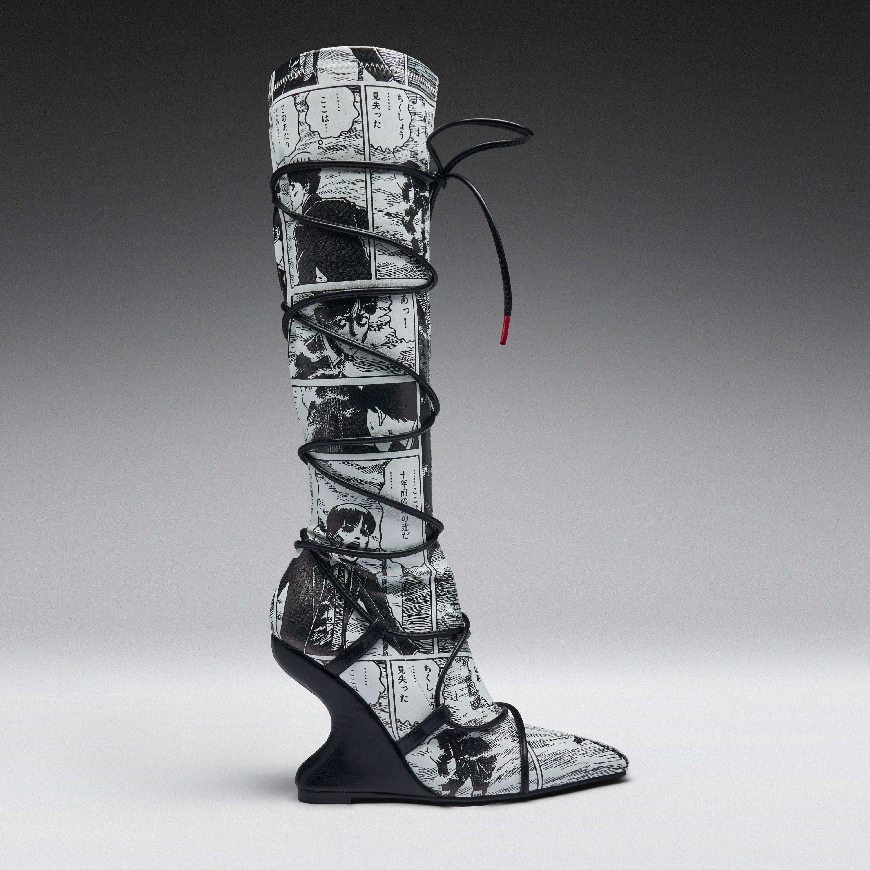A single tall knee-high boot with a black and white manga comic book print, wrapped in black lace up to the ankle, set against a dark-to-light gray gradient studio background.