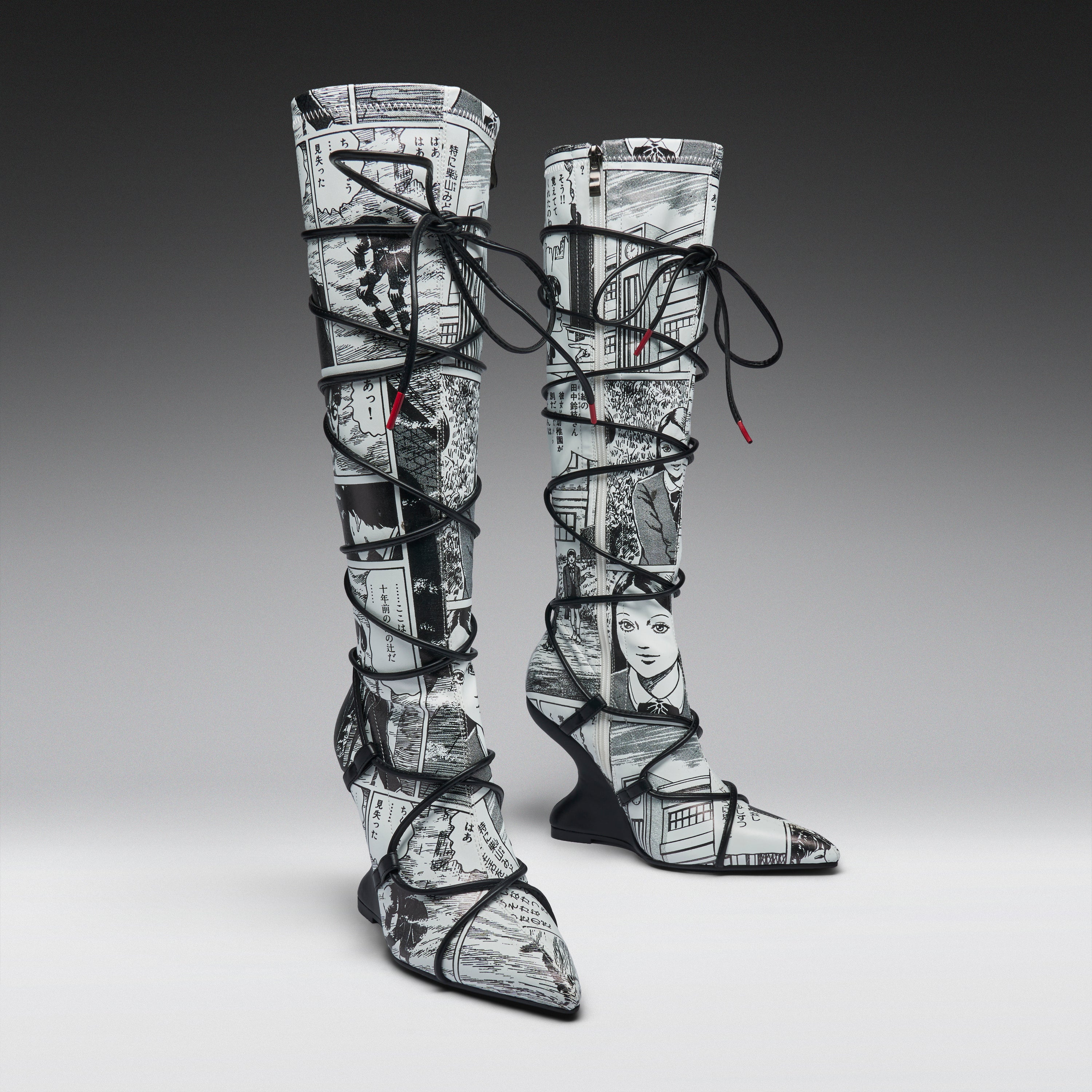 A pair of thigh-high pointed-toe boots with a black and white newspaper collage print, wrapped in black lace up to the ankles, shown on a gray gradient studio background.