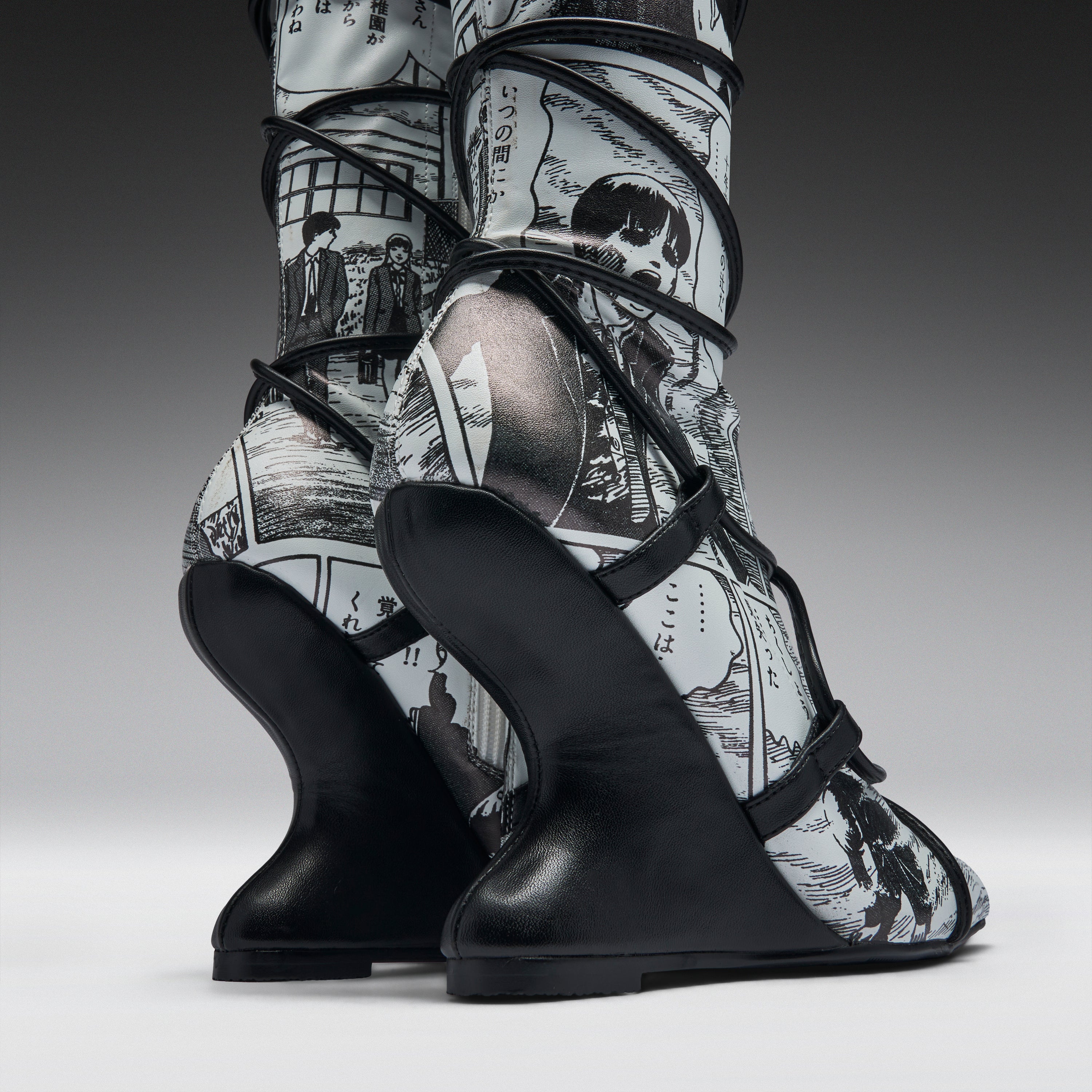 A pair of high-heeled boots with sculptural black wedge heels and black straps, featuring a black-and-white manga comic book print on the uppers, shown against a dark gray studio background.