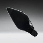 A black pointed-toe shoe shown from the sole side, featuring a textured black rubber outsole and a silver metallic side accent, set against a dark-to-light gray gradient background.