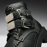Close-up of a black leather lace-up boot with three wide decorative straps, each featuring a large silver-tone metal plate and buckle, white contrast stitching, and a chunky black sole.