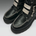Black leather lace-up boots with silver metal strap accents, white contrast stitching, and thick black soles, shown on a light gray background.