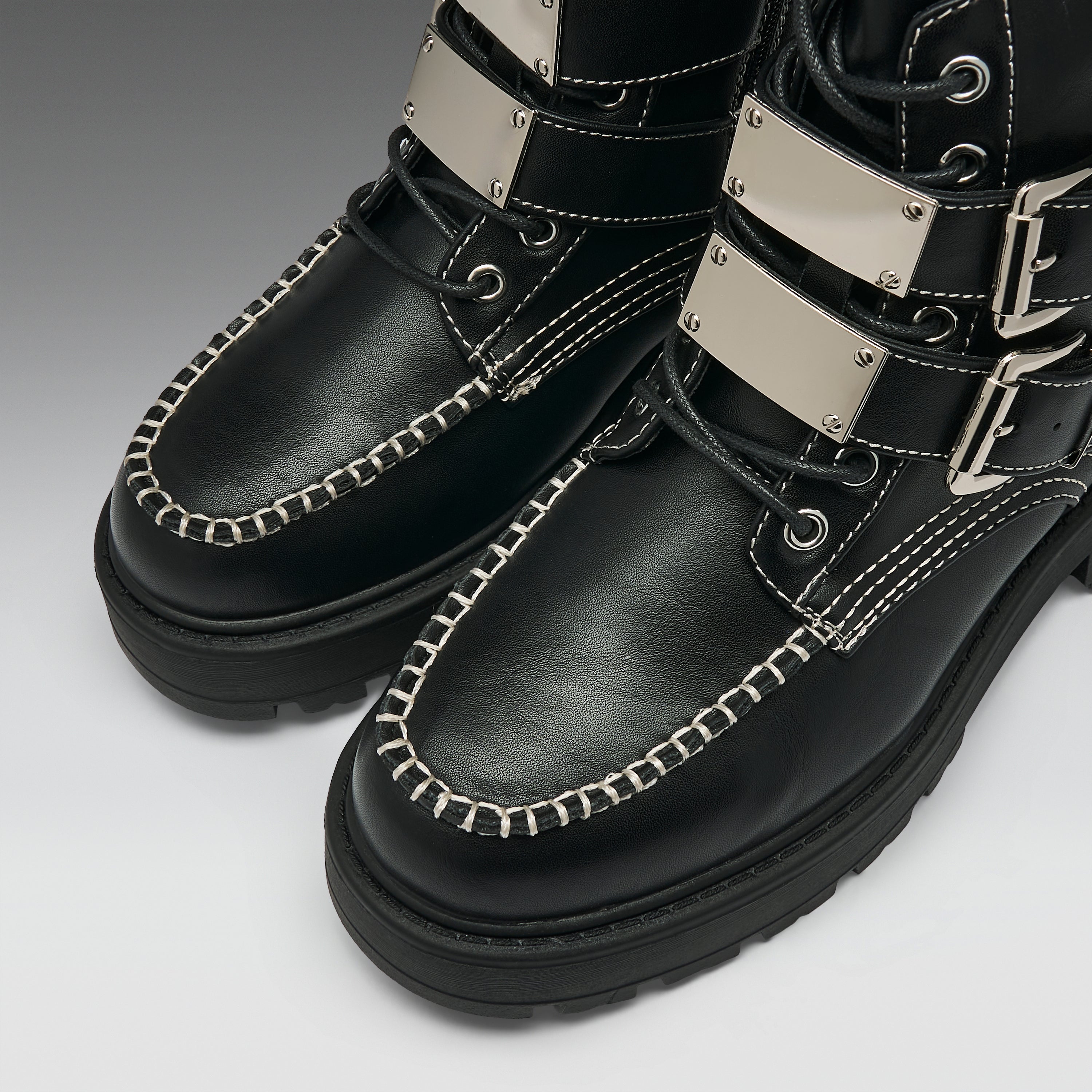 Black leather lace-up boots with silver metal strap accents, white contrast stitching, and thick black soles, shown on a light gray background.