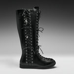 A single black leather knee-high lace-up boot with silver metal eyelets and decorative skull-and-crossbones laces, shown in profile against a dark gray studio background.