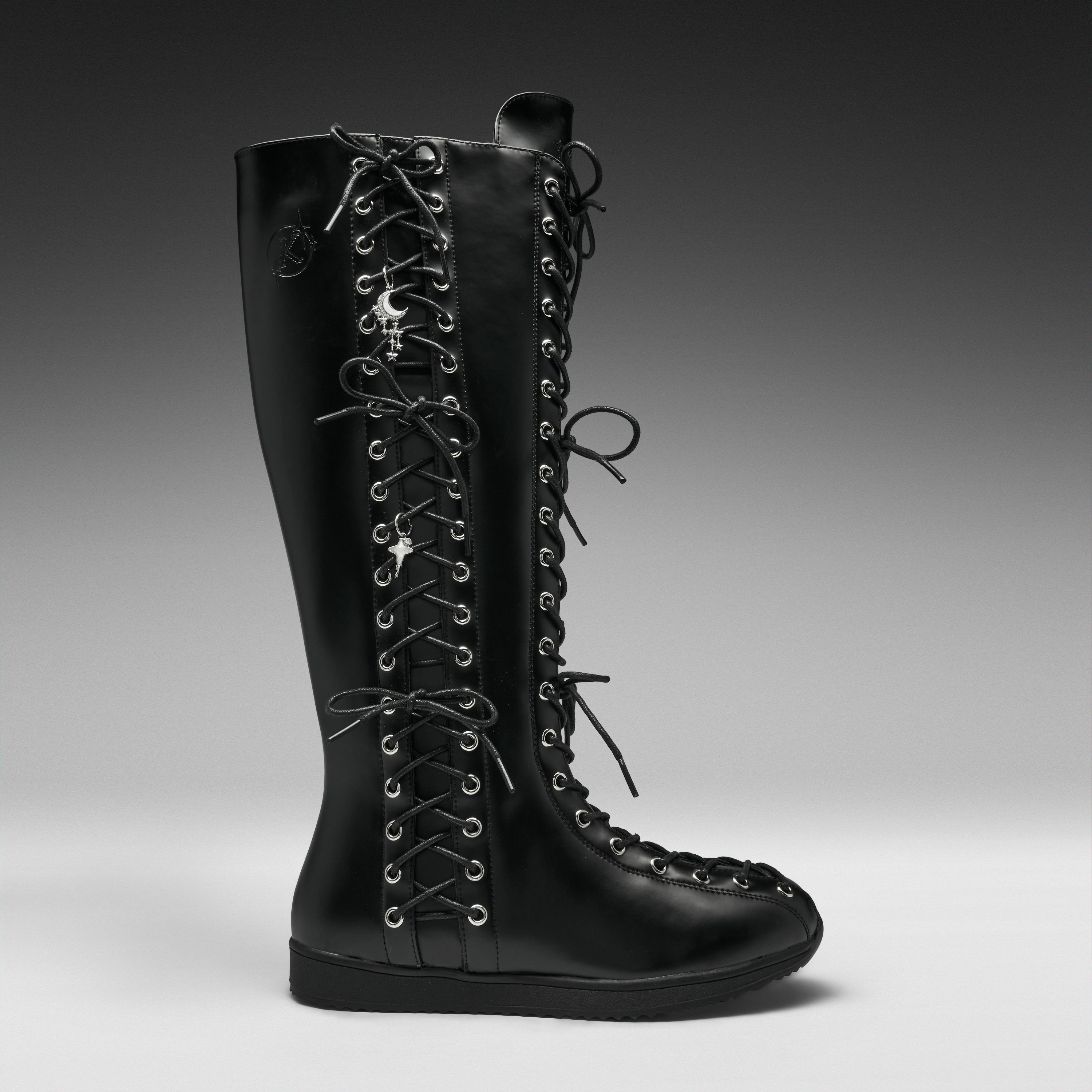 A single black leather knee-high lace-up boot with silver metal eyelets and decorative skull-and-crossbones laces, shown in profile against a dark gray studio background.