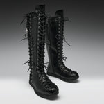 A pair of black leather knee-high lace-up boots with multiple decorative laces and silver-tone eyelets, photographed on a clean gray studio background.