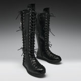 A pair of black leather knee-high lace-up boots with multiple decorative laces and silver-tone eyelets, photographed on a clean gray studio background.