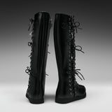 A pair of black knee-high lace-up boots shown from the back on a dark-to-light gray gradient studio background.
