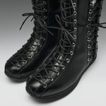 A pair of black leather lace-up boots with silver metal eyelets, shown on a neutral gray background.
