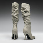 A pair of tall, knee-high heeled boots in a light gray suede-like material, shown from the back against a dark-to-light gray gradient studio background.