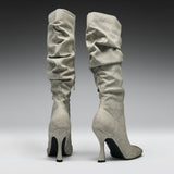 A pair of tall, knee-high heeled boots in a light gray suede-like material, shown from the back against a dark-to-light gray gradient studio background.