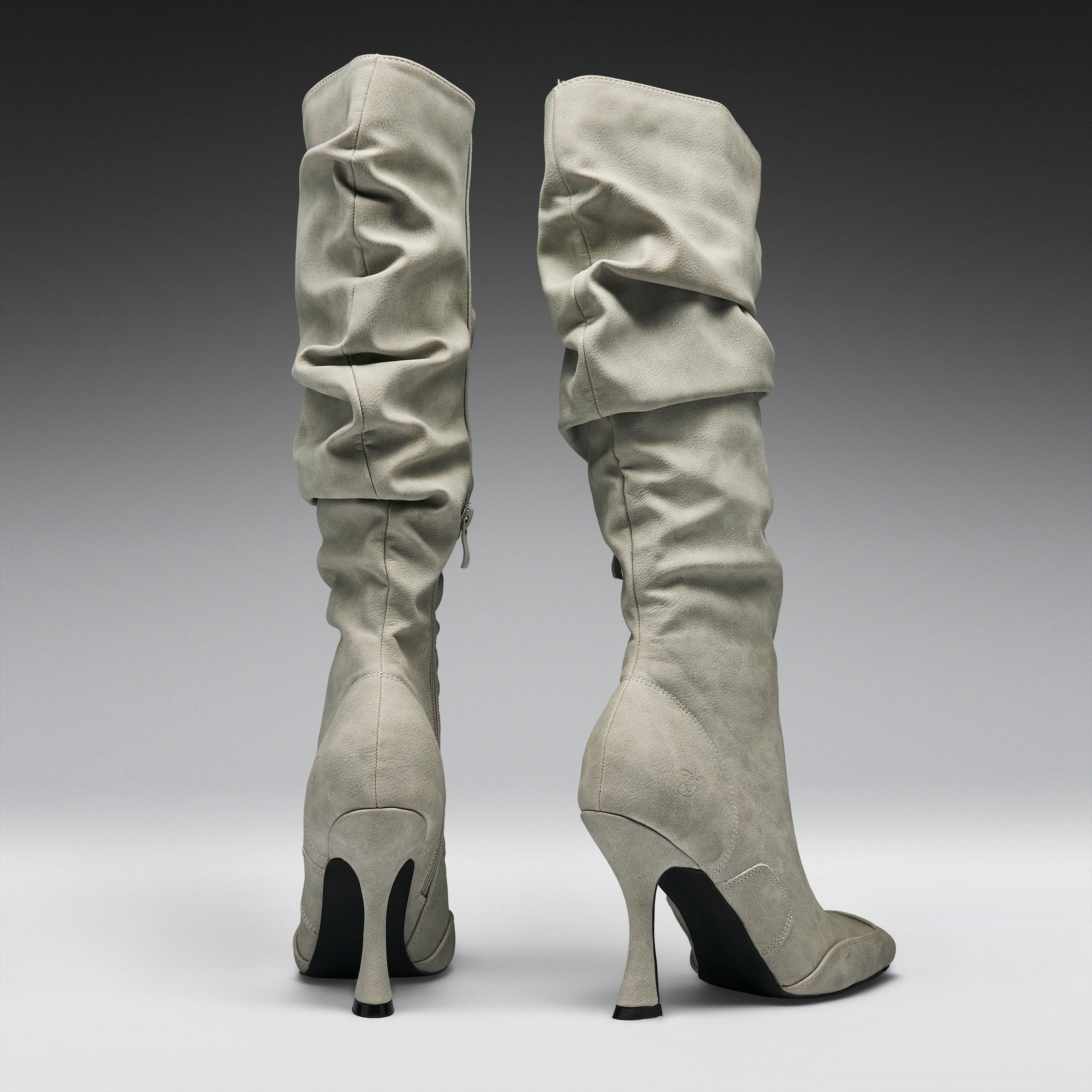 A pair of tall, knee-high heeled boots in a light gray suede-like material, shown from the back against a dark-to-light gray gradient studio background.