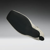 A close-up of a shoe's outsole and heel area, showing a black textured rubber tread and a light beige fabric heel cover with a small black pull tab, set against a dark-to-light gray gradient background.