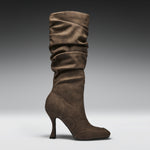 A single mid-calf heeled boot in brown suede, shown in profile against a dark-to-light gray gradient studio background.