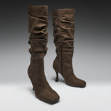 A pair of brown suede slouchy knee-high boots with kitten heels, shown on a neutral gray gradient studio background.