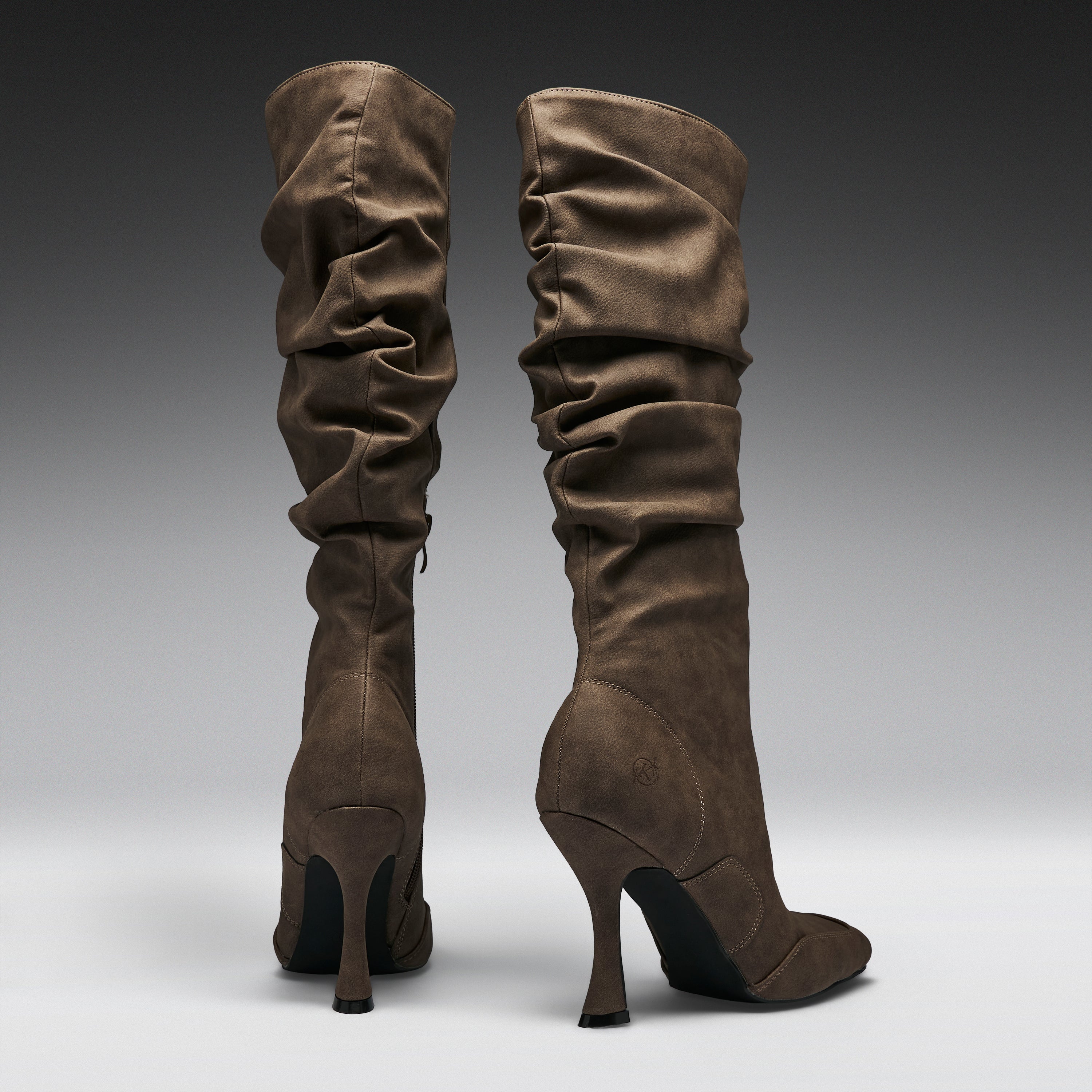 A pair of tall, slouchy knee-high boots in a dark brown suede-like material, shown from the back against a dark-to-light gray gradient studio background.