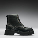 A single black leather lace-up boot with contrast white stitching, gold-tone eyelets, and a chunky lug sole, photographed on a dark-to-light gray gradient studio background.