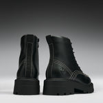 A pair of black leather lace-up ankle boots with chunky lug soles, shown from the back and side against a dark gray gradient background.