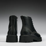 A pair of black leather lace-up ankle boots with chunky lug soles, shown from the back and side against a dark gray gradient background.