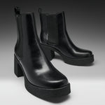 A pair of black leather Chelsea-style ankle boots with platform soles and block heels, photographed on a clean gray studio background.