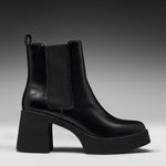 A black leather ankle boot with a chunky block heel and platform sole, featuring a black elastic side panel and a small embossed logo on the side.