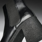 Close-up of a black leather ankle boot with a chunky textured block heel and a tonal embossed logo on the side.