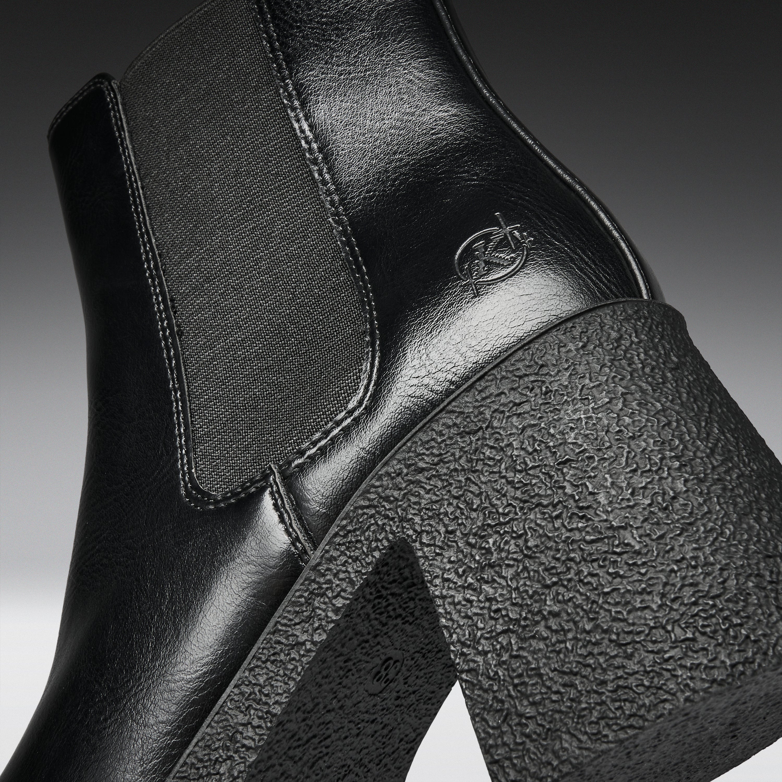 Close-up of a black leather ankle boot with a chunky textured block heel and a tonal embossed logo on the side.