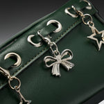 Close-up of a dark green textured leather bag featuring silver-tone metal grommets and dangling charms, including a bow-shaped charm and a star-shaped charm.