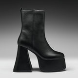 A single black leather ankle boot with a chunky, sculptural high block heel and a thick platform sole, shown from a side profile against a dark gray gradient studio background.