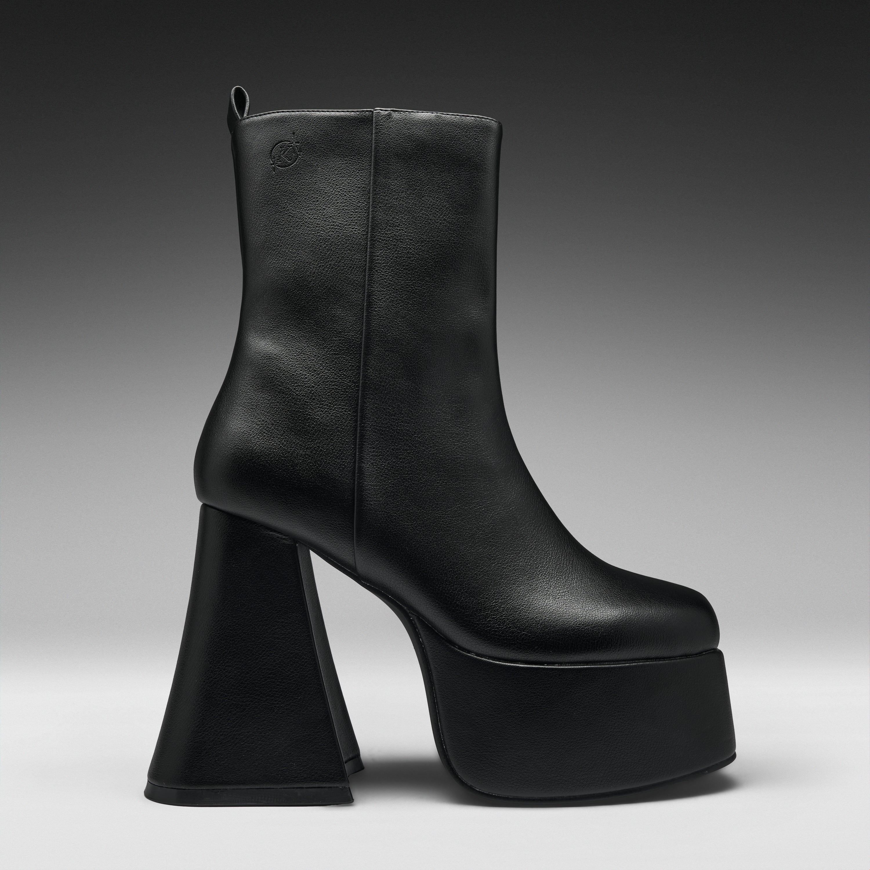 A single black leather ankle boot with a chunky, sculptural high block heel and a thick platform sole, shown from a side profile against a dark gray gradient studio background.