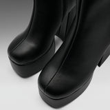 Close-up of a pair of black leather platform ankle boots with a chunky block heel, showing the toe and side profile against a neutral gray background.